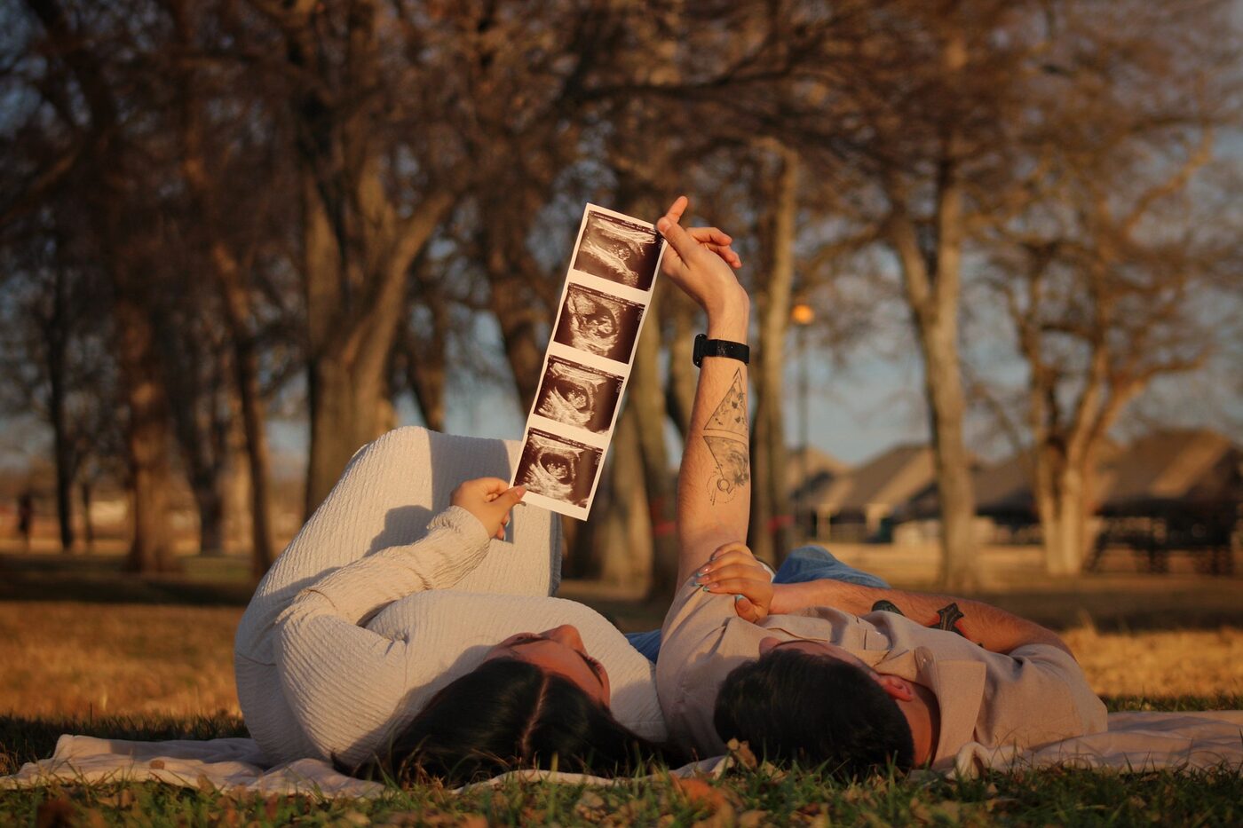 Couple lying in the grass holding up ultrasound photo